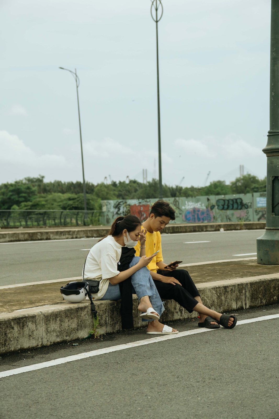 Hai người trẻ ngồi lề đường cùng xem điện thoại