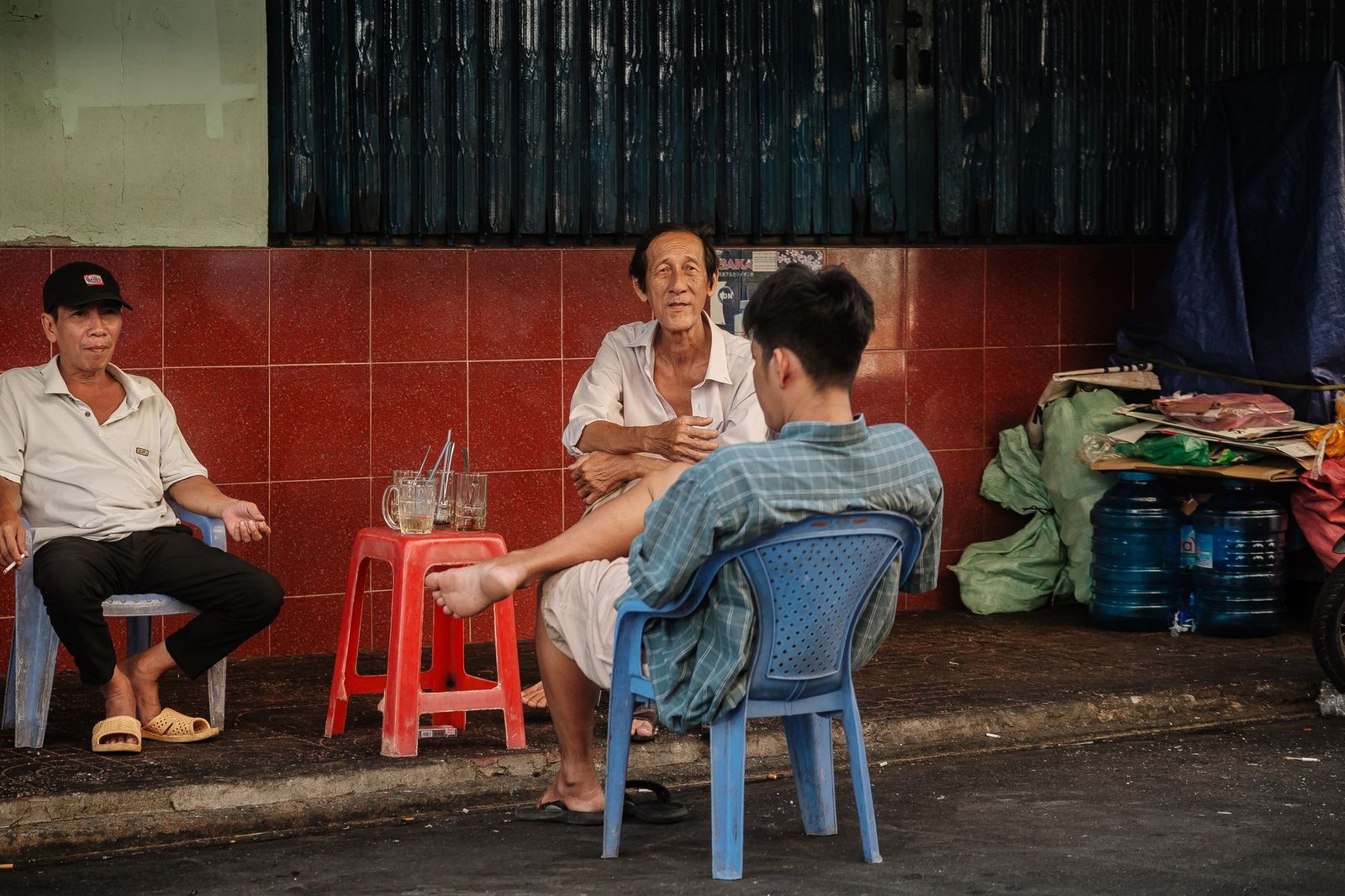 Mấy người ngồi ghế nhựa trò chuyện bên hè phố Việt Nam